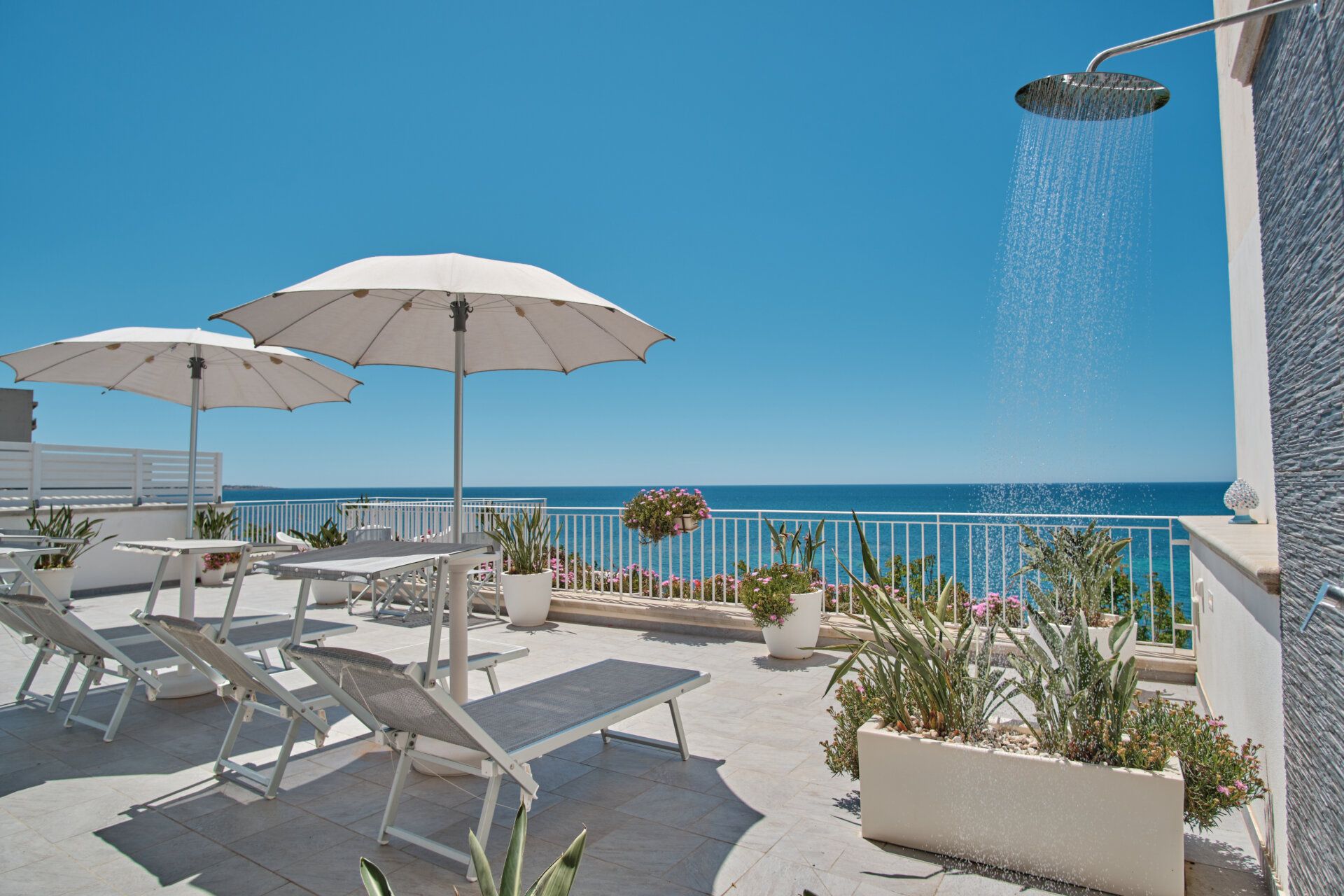 Lettini, ombrellone e una doccia esterna sulla terrazza, con il mare alle spalle — Sunset Terrace Mazara del Vallo